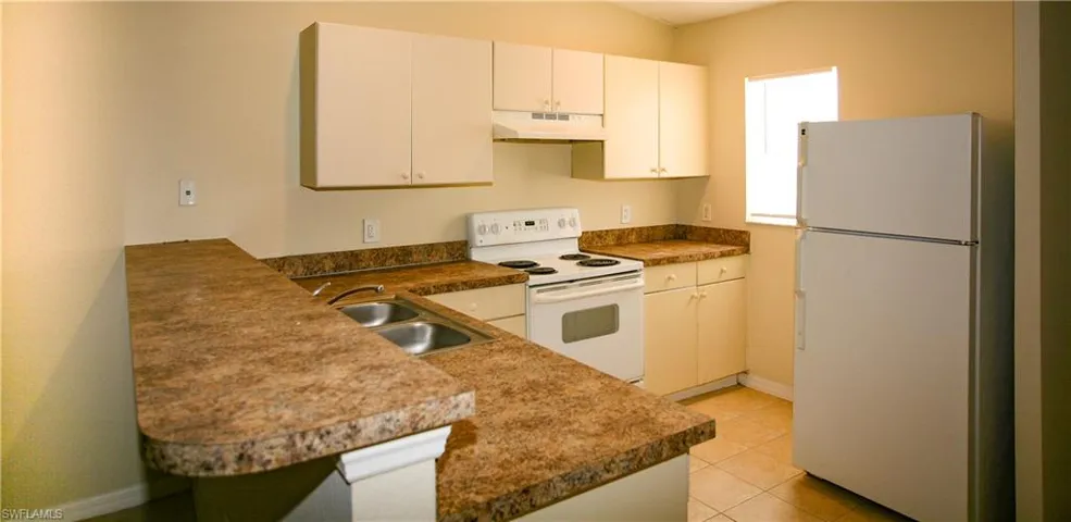 The kitchen features light-colored cabinetry, a double basin sink, and white appliances including a refrigerator and an oven