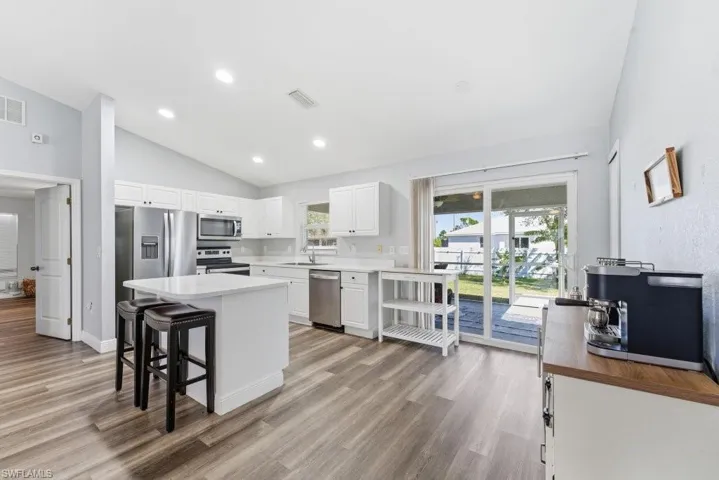 Kitchen featuring white cabinetry, vaulted ceiling, a kitchen island, stainless steel appliances, and a kitchen breakfast bar