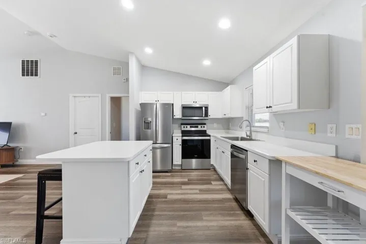 Kitchen featuring stainless steel appliances, a kitchen bar, white cabinetry, dark wood-type flooring, and vaulted ceiling