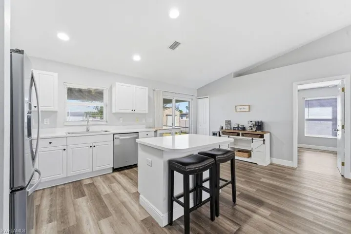 Kitchen with a kitchen island, white cabinets, stainless steel appliances, a breakfast bar area, and light wood finished floors