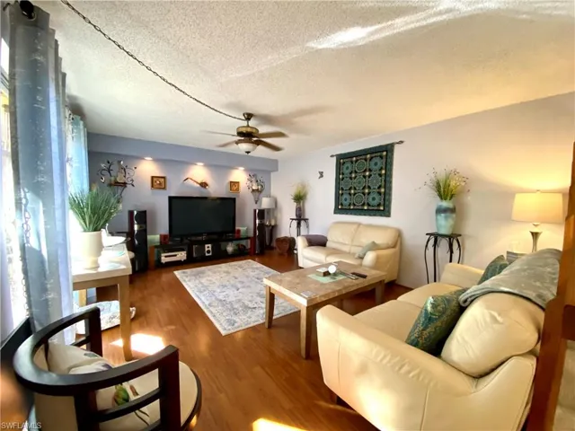 Living room with wood-type flooring, a textured ceiling, and ceiling fan