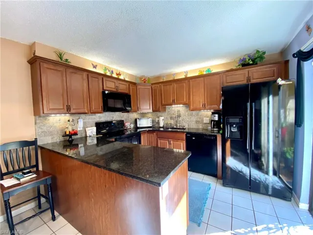 Kitchen with sink, light tile patterned floors, dark stone countertops, kitchen peninsula, and black appliances