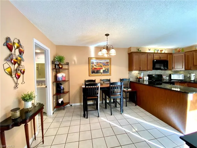 Kitchen featuring tasteful backsplash, hanging light fixtures, black appliances, and light tile patterned flooring