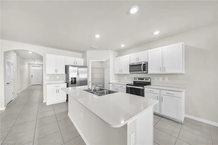Kitchen featuring white cabinets, stainless steel appliances, arched walkways, a kitchen island with sink, and recessed lighting