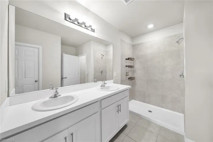 Bathroom with light tile patterned flooring, a stall shower, and double vanity