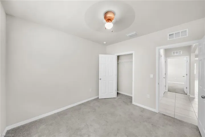 Unfurnished bedroom with light carpet, ceiling fan, a closet, and light tile patterned floors