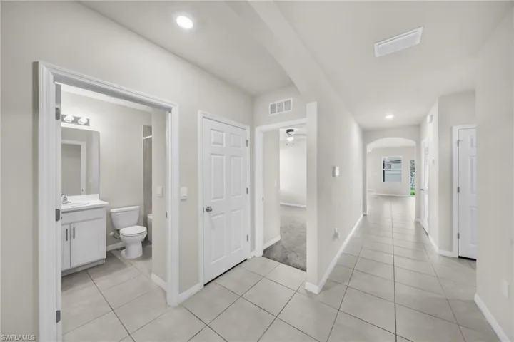 Hall with arched walkways, light tile patterned floors, and recessed lighting
