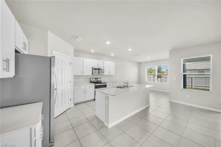 Kitchen with recessed lighting, appliances with stainless steel finishes, an island with sink, light tile patterned flooring, and white cabinetry