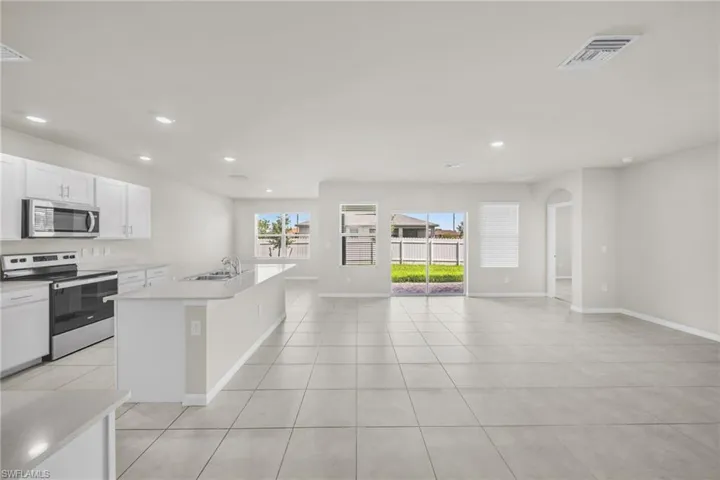 Kitchen featuring appliances with stainless steel finishes, a kitchen island with sink, white cabinetry, light tile patterned flooring, and open floor plan