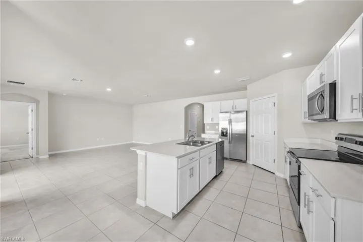 Kitchen with arched walkways, stainless steel appliances, white cabinets, recessed lighting, and an island with sink