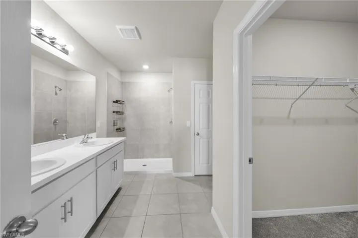 Full bathroom featuring a stall shower, light tile patterned floors, double vanity, and a walk in closet