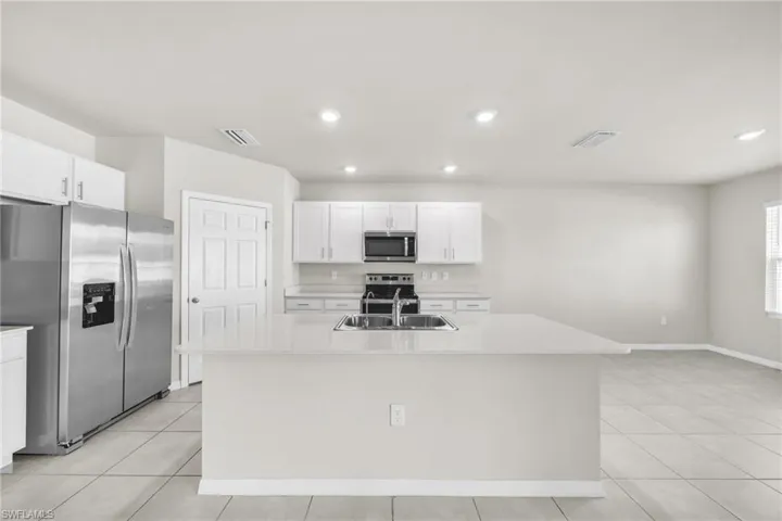Kitchen featuring stainless steel appliances, an island with sink, white cabinets, light tile patterned floors, and recessed lighting