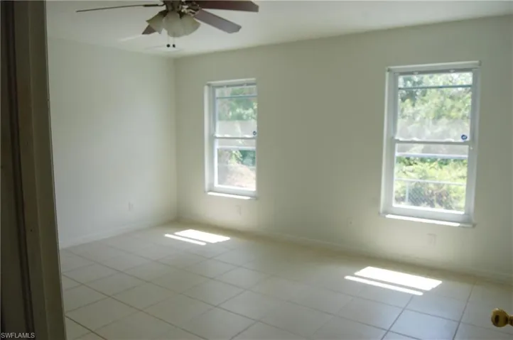 Empty room featuring ceiling fan, a wealth of natural light, and light tile patterned floors