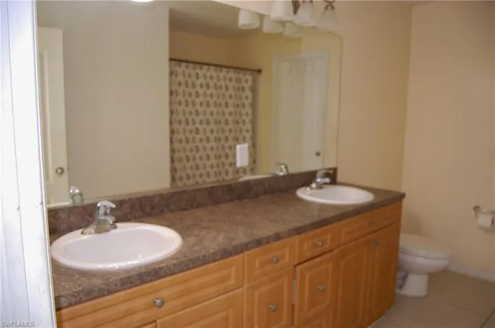 Bathroom featuring toilet, tile patterned flooring, and dual bowl vanity