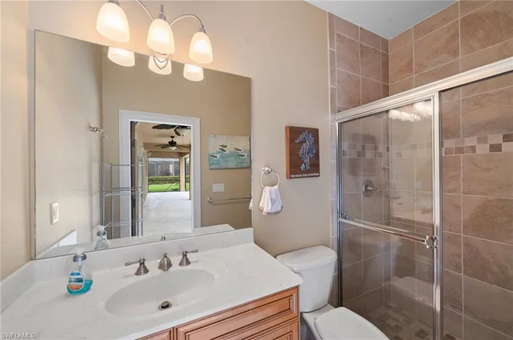 Bathroom featuring ceiling fan, a shower with door, vanity, and toilet