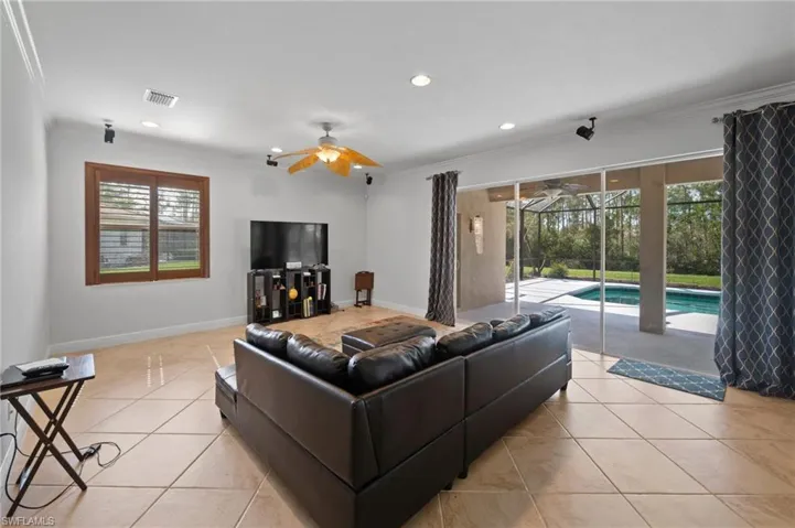 Living room featuring light tile patterned floors, ceiling fan, and crown molding
