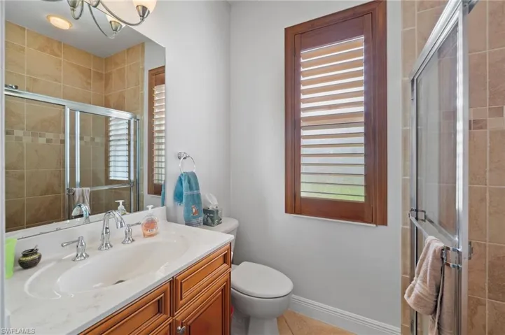 Bathroom featuring tile patterned floors, a shower with door, vanity, a notable chandelier, and toilet