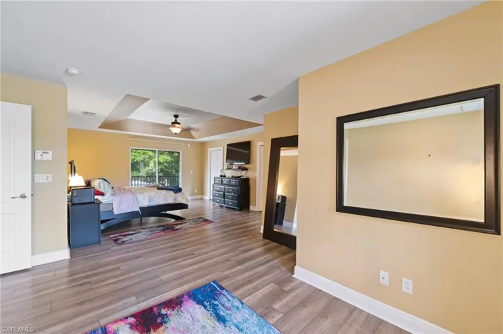 Bedroom with light hardwood / wood-style floors, ceiling fan, and a raised ceiling