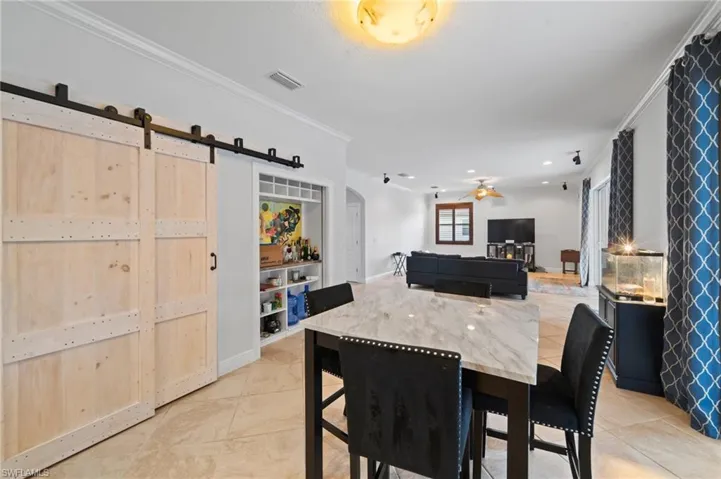 Dining room with a barn door, ceiling fan, light tile patterned floors, and crown molding