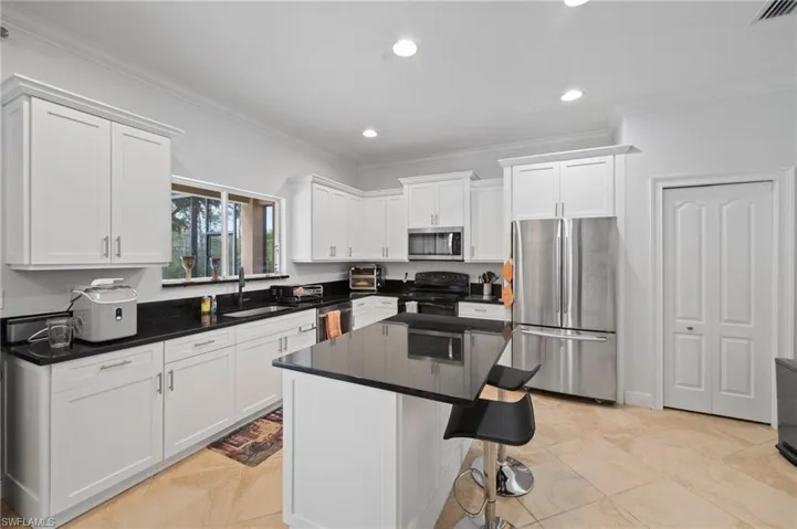 Kitchen with stainless steel appliances, a kitchen bar, white cabinetry, and a kitchen island