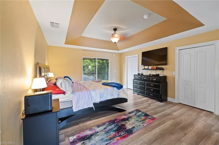 Bedroom with light wood-type flooring, ceiling fan, and a raised ceiling