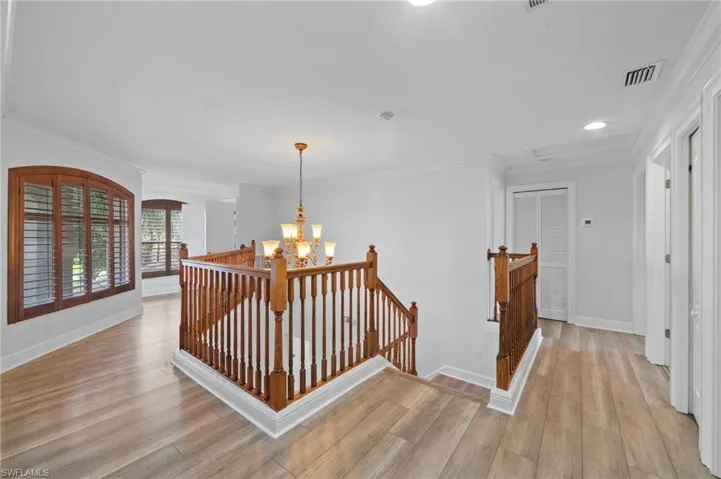 Corridor with light hardwood / wood-style flooring, a chandelier, and crown molding