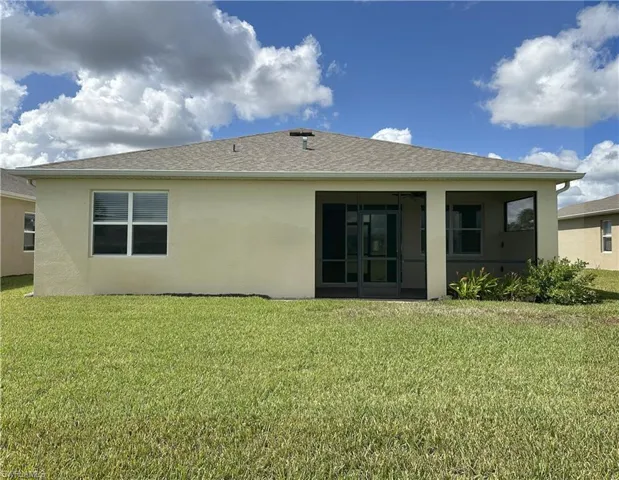 Back of property with stucco siding, a yard, roof with shingles, and a sunroom