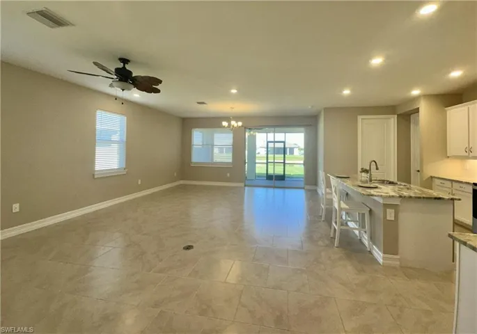 Kitchen with white cabinets, light stone counters, a center island with sink, recessed lighting, and a kitchen bar