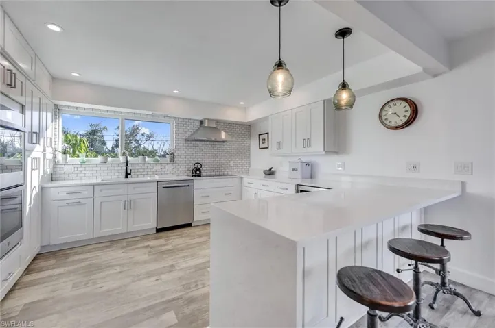Kitchen with a kitchen breakfast bar, a peninsula, light wood-style flooring, stainless steel appliances, and pendant lighting
