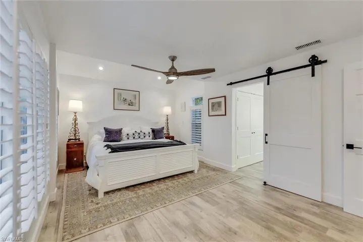 Bedroom with a barn door, light wood-style floors, ceiling fan, recessed lighting, and lofted ceiling