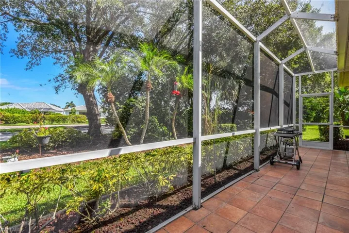 Screened patio with terracotta tile flooring, offering expansive views of mature trees and landscaping