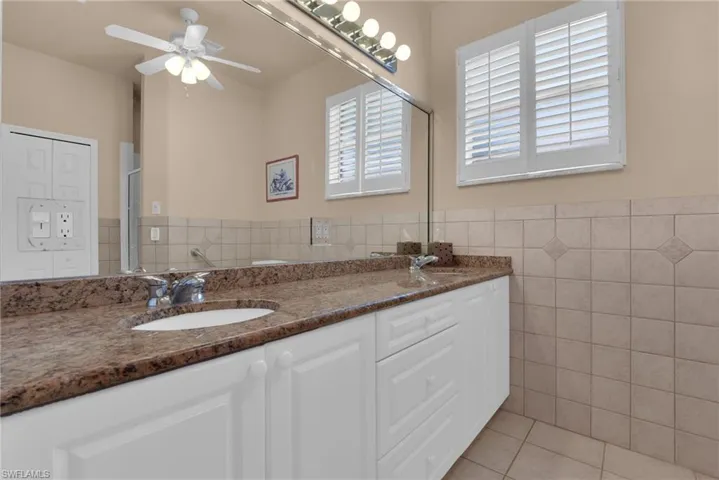 Bathroom vanity featuring a granite countertop, dual undermount sinks, and white shaker-style cabinetry