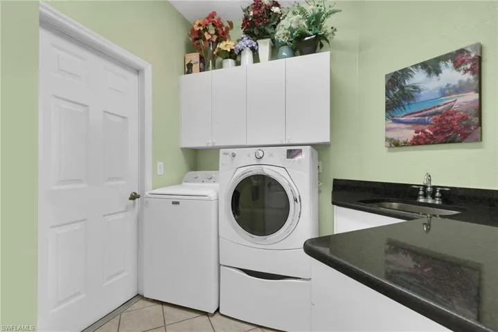 Functional laundry area featuring white shaker-style cabinetry, dark stone countertops, and a stainless steel undermount sink