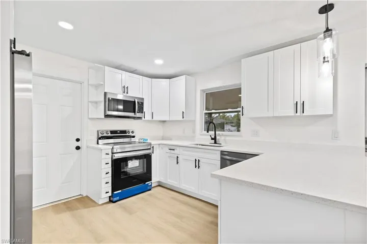 Kitchen with stainless steel appliances, sink, pendant lighting, light wood-type flooring, and white cabinets