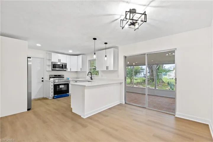 Kitchen with appliances with stainless steel finishes, sink, light wood-type flooring, kitchen peninsula, and white cabinetry