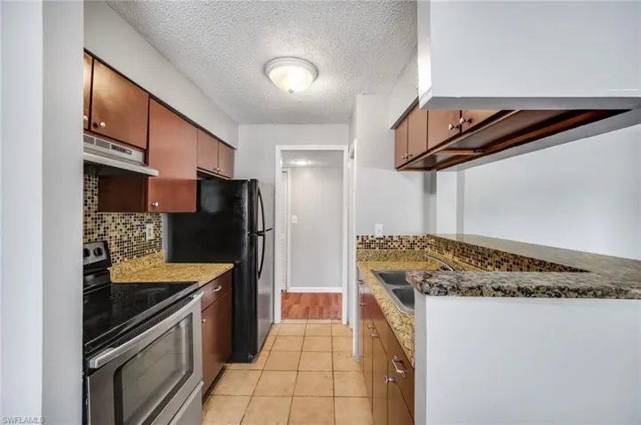 Kitchen with stainless steel range with electric stovetop, a textured ceiling, decorative backsplash, light tile patterned flooring, and dark stone countertops