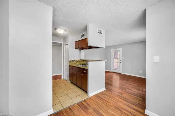 Kitchen with a textured ceiling, light wood-type flooring, and dark stone counters