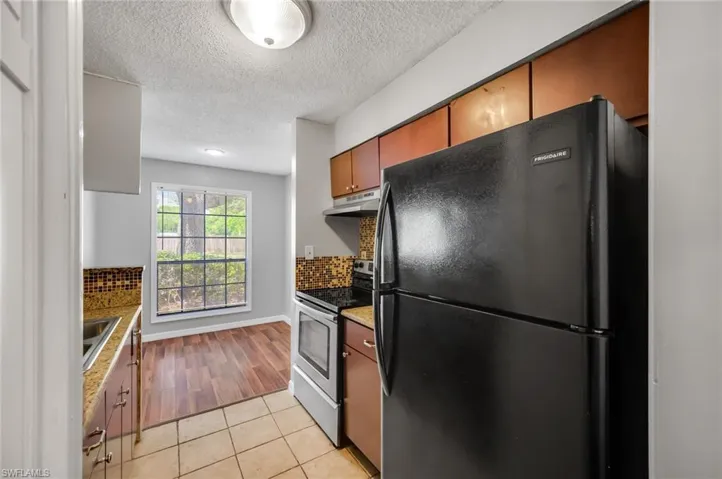 Kitchen featuring freestanding refrigerator, stainless steel electric range, light tile patterned floors, decorative backsplash, and a textured ceiling