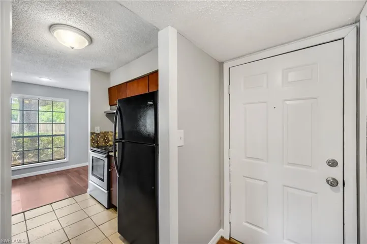 Kitchen with freestanding refrigerator, a textured ceiling, light tile patterned floors, stainless steel electric range oven, and brown cabinets