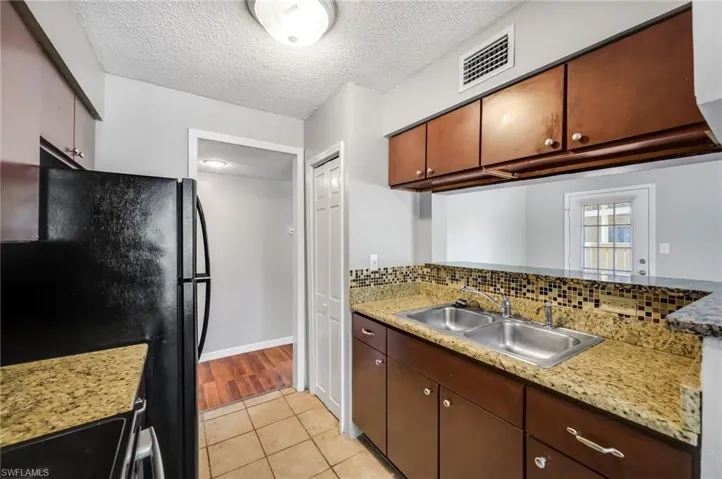 Kitchen with a textured ceiling, light tile patterned floors, black / electric stove, and light stone countertops
