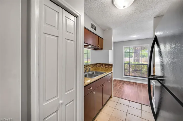 Kitchen with freestanding refrigerator, light tile patterned floors, a textured ceiling, and dark stone countertops