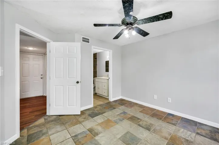 Unfurnished bedroom featuring a textured ceiling, ensuite bathroom, a ceiling fan, and stone tile floors