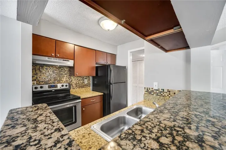 Kitchen featuring stainless steel range with electric cooktop, decorative backsplash, freestanding refrigerator, under cabinet range hood, and a textured ceiling