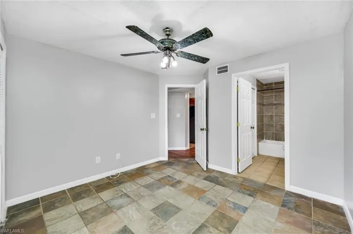 Unfurnished bedroom with light stone finish floors, a ceiling fan, and ensuite bath