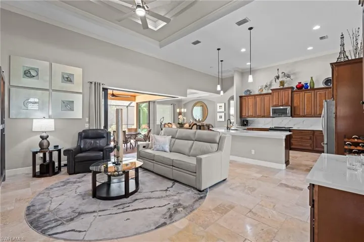 Living room with crown molding, visible vents, a ceiling fan, and stone tile floors