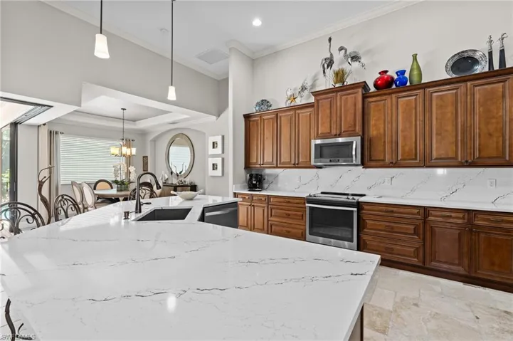 Kitchen featuring appliances with stainless steel finishes, ornamental molding, a kitchen island with sink, decorative backsplash, and a sink