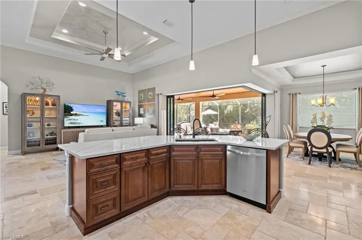 Kitchen featuring a raised ceiling, stainless steel dishwasher, a sink, and stone tile flooring