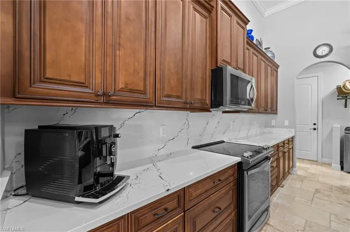 Kitchen featuring ornamental molding, backsplash, light stone countertops, stainless steel appliances, and stone tile floors
