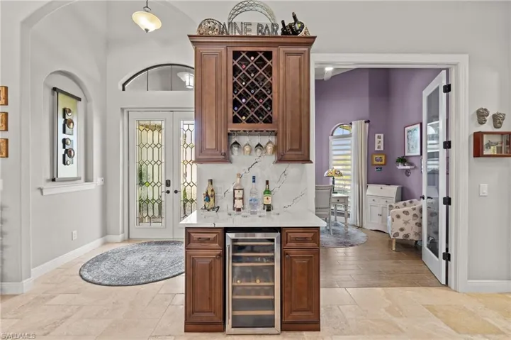 Bar featuring a bar, french doors, beverage cooler, and stone tile flooring