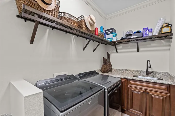 Clothes washing area featuring a sink, ornamental molding, independent washer and dryer, and cabinet space